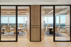 an office with glass walls and wooden flooring, overlooking the cityscape through large sliding doors