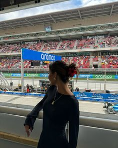 a woman standing in front of a race track looking out at the stands and cars