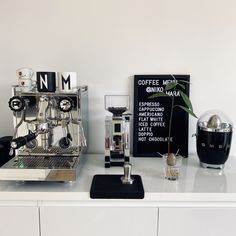 two espresso machines sitting on top of a white counter next to a black sign