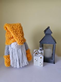 a knitted gnome next to a lantern and candle holder on a white tablecloth