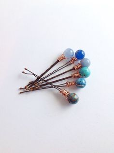 four different colored beads are on top of some brown hair pins with wire wrapped around them