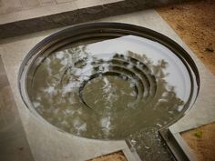 a water fountain with trees reflected in it's reflection on the ground next to a sidewalk