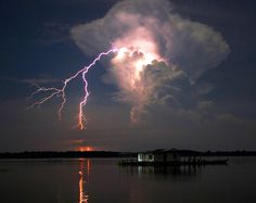 a lightning bolt hitting over a house in the middle of a body of water at night