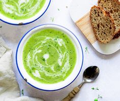 two bowls filled with green soup next to slices of bread