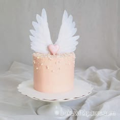 a pink cake with white angel wings and a heart decoration on the top is sitting on a plate