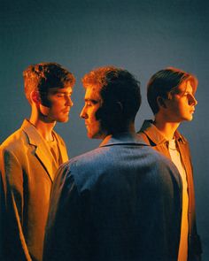 three men standing next to each other in front of a blue background with one man looking at the other