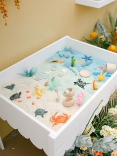 an ocean themed sand tray with sea animals and seashells on it in front of flowers