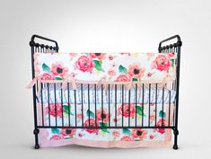 a baby crib with pink and red flowers on the bedding, next to a white wall