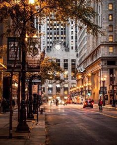 an empty city street at night with tall buildings in the background and people walking on the sidewalk