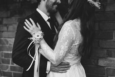 a bride and groom standing in front of a brick wall with their arms around each other