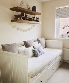 a white daybed with pillows and stuffed animals on it in a small room next to a window