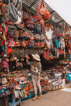 a woman standing in front of a store with lots of hats and scarves on display