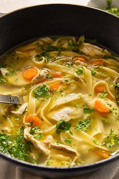 a pot full of chicken noodle soup with carrots and parsley on the side