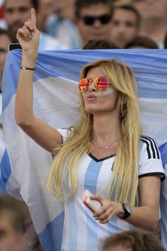 a woman wearing sunglasses and holding a flag in her hand at a soccer game with people watching from the stands