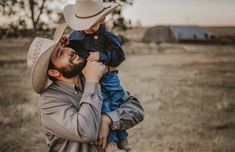 a man holding a small child wearing a cowboy hat in the middle of a field