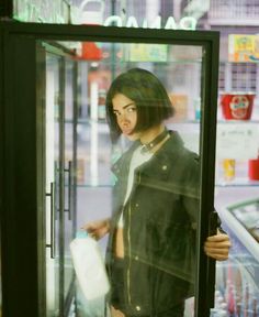 a woman standing in front of a store window with her hand on the door handle