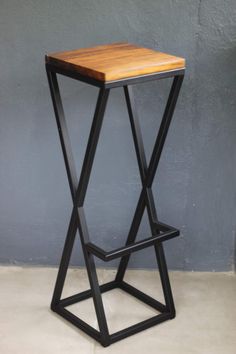 a wooden stool sitting on top of a cement floor next to a gray wall and black metal frame