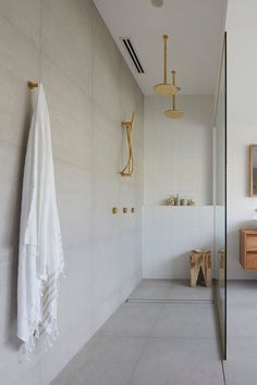 a white bathroom with gold fixtures and towels hanging on the wall, along with a mirror