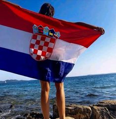 a person standing on rocks with a flag in their hands and the ocean behind them