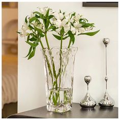 a glass vase with white flowers in it on a table next to two spoons