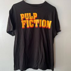 a black t - shirt with the word pulp fiction printed in orange and yellow on it