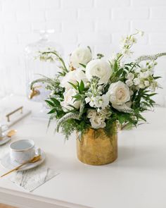 a vase filled with white flowers sitting on top of a table next to a cup and saucer