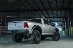 a silver truck is parked in an empty garage with its lights on and it's big tires