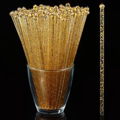 a glass vase filled with gold glitter next to a golden stick on a black background