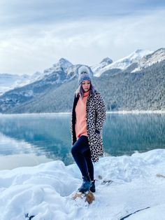 a woman standing on top of a snow covered slope next to a body of water