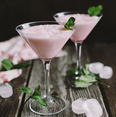 two martini glasses filled with pink liquid and mint garnish on a wooden table