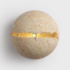 a round object with a gold strip on it's side, sitting on a white surface