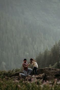 a man kneeling down next to a woman on top of a hill with trees in the background