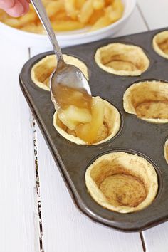 a person spooning some food out of a muffin tin with apples in it