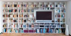 a living room filled with lots of books and a flat screen tv mounted on a wall