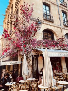 an outdoor cafe with tables and umbrellas in front of the building that has flowers on it