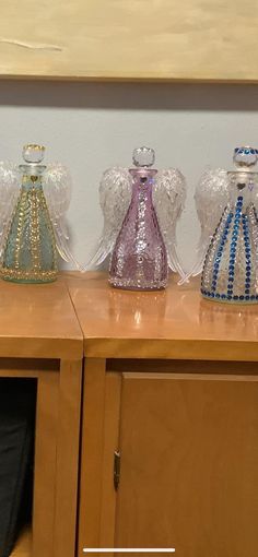 three glass vases sitting on top of a wooden table next to a wall mounted painting