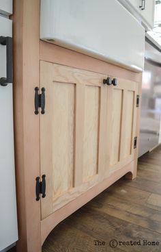 an unfinished kitchen cabinet with black handles and knobs on the door, next to a white refrigerator