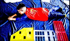 a young boy laying on top of a bed covered in blue sheets and paper houses