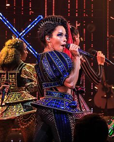 a group of women on stage with microphones in their hands and lights behind them