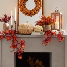 a mantel decorated with fall leaves and pumpkins, candles and a wreath on top