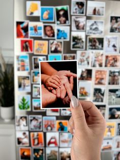 a person holding up a polaroid in front of a wall with pictures on it