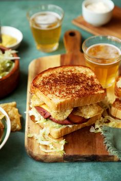 there is a sandwich on a cutting board with some beer and other food items around it