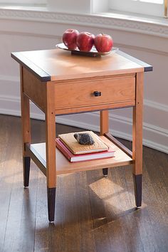 a wooden table with two apples on top and a book on the end shelf next to it