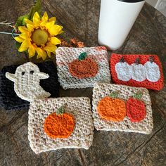 four crocheted coasters with pumpkins and ghost on them next to a sunflower