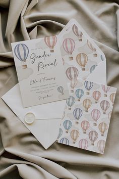 two cards with hot air balloons on them are laying on a bed sheet that is covered in fabric