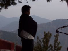 a man standing on top of a mountain next to a forest