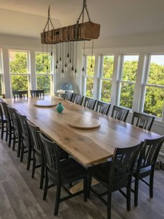 a large wooden dining table surrounded by black chairs and hanging chandelier over it