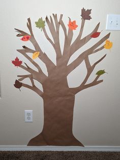 a tree made out of brown paper with fall leaves on it and an electrical outlet