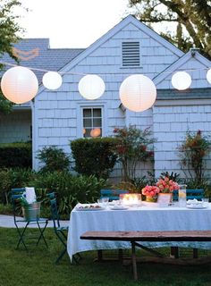 an outdoor dinner table with paper lanterns hanging from it's ceiling and lit candles on the table