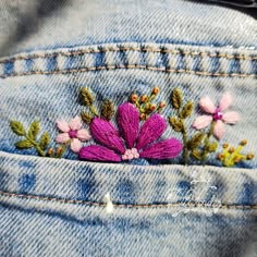 a pink flower is embroidered on the back of a pair of blue jean pants,